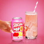 a hand holding a can of Strawberry Lemon Social Pop next to a poured glass with ice.